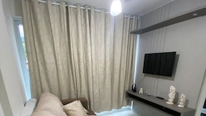 Una sala de estar moderna con un sofá, un ventilador de techo, un televisor de pantalla plana montado en la pared y una ventana con cortinas.