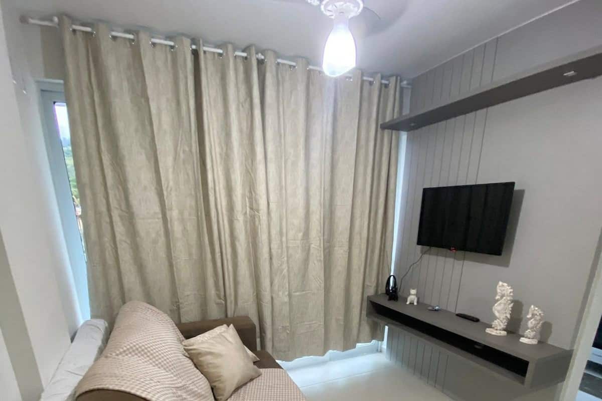 Un salon moderne avec un canapé, un ventilateur de plafond, un téléviseur à écran plat fixé au mur et une fenêtre avec des rideaux.