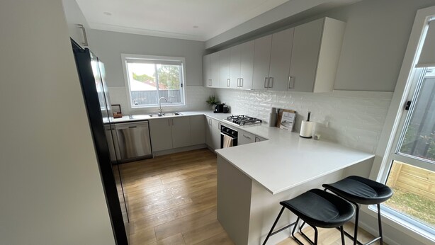 Een moderne keuken met witte kasten, een centraal eiland met barstoelen, een raam en uitzicht op de omgeving.