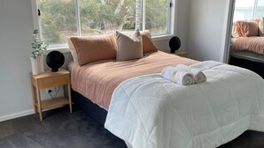 Een slaapkamer met een groot bed, een nachtkastje, een raam en een plafondventilator.