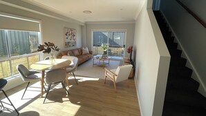 Een ruime woonkamer met een bank, salontafel en stoelen, een eethoek met een tafel en stoelen, en een trap.