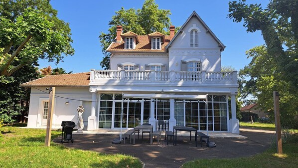 Une maison à deux étages avec un balcon, de grandes fenêtres et une statue dans le jardin.