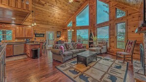Una cabaña espaciosa con una amplia sala de estar, pisos de madera y ventanas múltiples que ofrecen vistas al exterior.