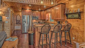 Interior de una cabaña de madera con cocina, taburetes de bar y una mesa de comedor.