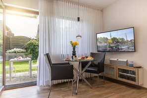 A modern hotel room with a dining area, a TV, and a view of a marina. - Ferienwohnung 50050 - Helle Erdgeschoss- Ferienwohnung (komplett in 2023 Renoviert und neu (Wittmund)