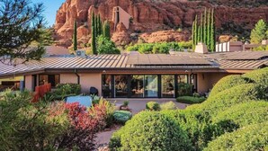 A modern house with a flat roof, surrounded by lush greenery and red rock formations in the background. - Chapel Vista Home With Stunning Views of Red Rocks & Chapel. Hot-Tub & Gardens. (Sedona)