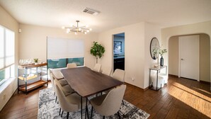Un comedor moderno con una mesa de madera oscura, sillas color beige, una mesa baja de vidrio y una planta en maceta.