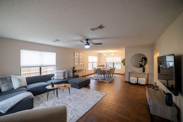 A spacious living room with a gray sofa, a coffee table, and a dining area with a table and chairs.