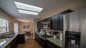 Una cocina moderna con armarios oscuros, encimeras de granito, electrodomésticos de acero inoxidable y un tragaluz.