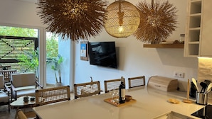 Eine moderne Küche mit einer großen Kochinsel, hängenden Pendelleuchten und einem flachbildfernseher an der Wand.