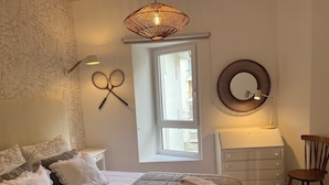Ein Schlafzimmer mit einem Bett, zwei an der Wand befestigten Tennisschlägern, einem Fenster, einem Schminktisch und einem Stuhl.