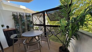 Ein Balkon mit rundem Tisch und zwei Stühlen, umgeben von Topfpflanzen und einem Holzboden.