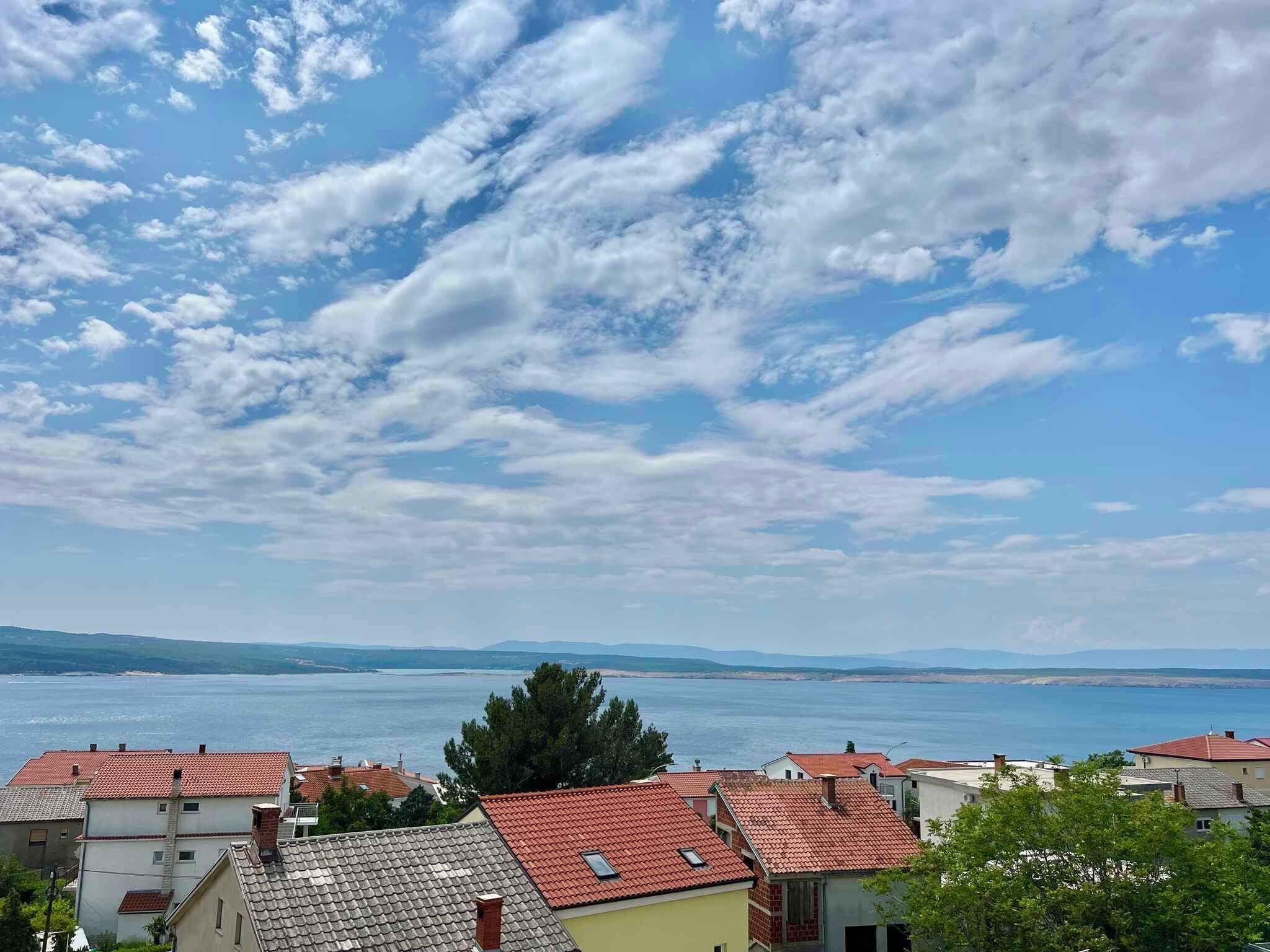 En kystby med røde tegltage, havudsigt og en klar himmel med spredte skyer.