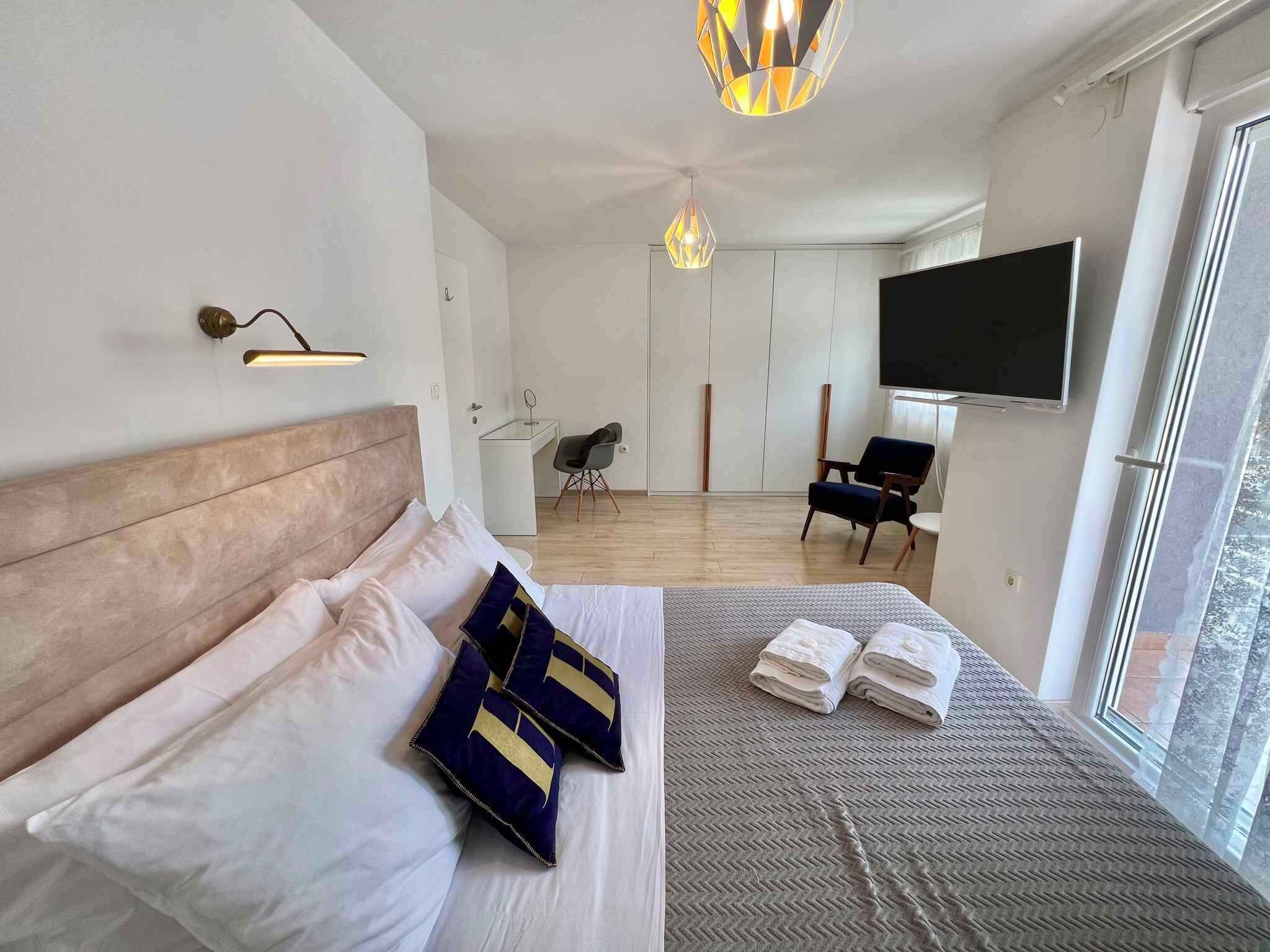 A modern bedroom with a large bed, a desk, a chair, and a TV.
