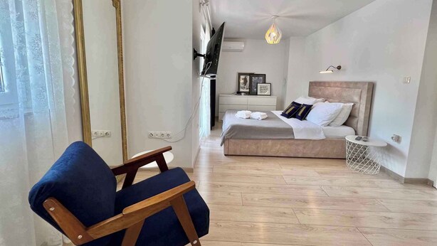 A modern bedroom with a large bed, a chair, a TV, and a chandelier. - Holiday apartment with balcony and air conditioning (Crikvenica)