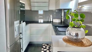 A modern kitchen with white cabinets, a black countertop, and a small potted plant on a woven placemat. - Holiday apartment with balcony and air conditioning (Crikvenica)