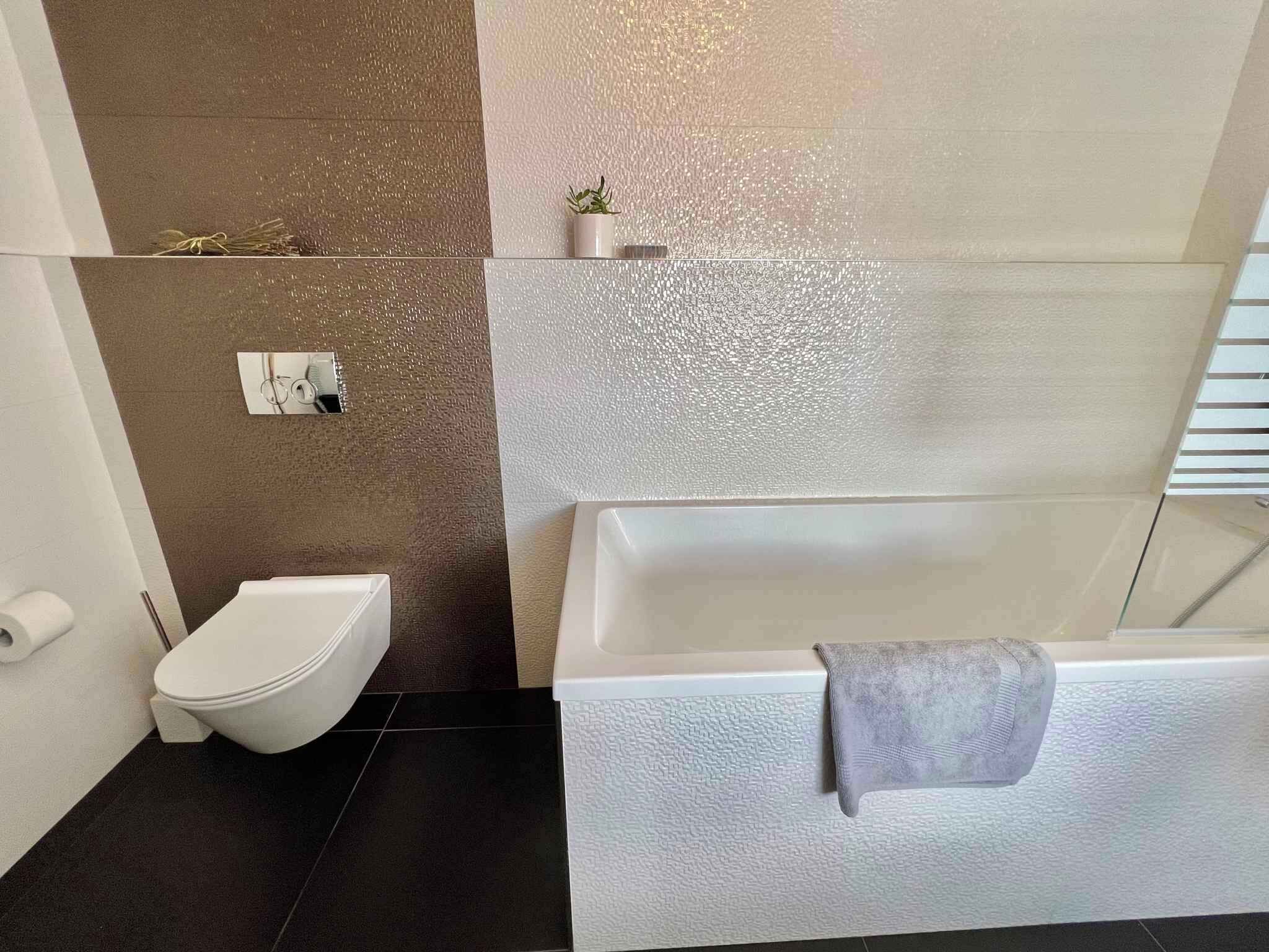 Une salle de bain moderne avec des toilettes blanches, une baignoire avec une serviette et un mur à motifs.