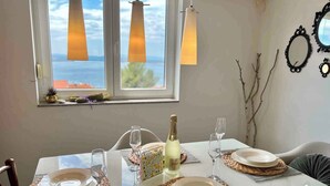 A dining table set with plates, glasses, and a bottle of champagne, with a view of the sea through a window. - Holiday apartment with balcony and air conditioning (Crikvenica)