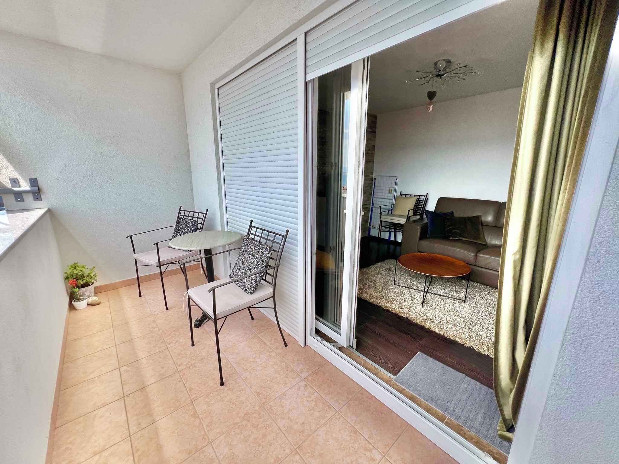 A balcony with a table and chairs, a sliding glass door leading to a living room with a sofa and a coffee table.