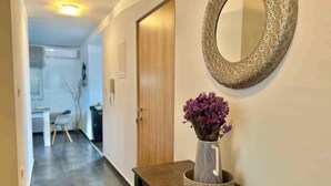 A hallway with a wooden door, a round mirror, and a vase with purple flowers on a dark wooden table. - Holiday apartment with balcony and air conditioning (Crikvenica)