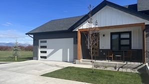 Een modern herenhuis met garage, overdekte veranda en een kleine boom in de voortuin.