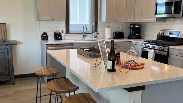 Een moderne keuken met een groot eiland, barstoelen, een koffiezetapparaat en een magnetron.