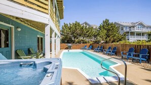 Une piscine avec un jacuzzi, entourée de chaises Adirondack bleues et d’une terrasse en bois.