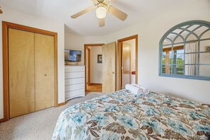 Een slaapkamer met een bed, een plafondventilator, een kledingkast, een dressoir en een raam met gordijnen.