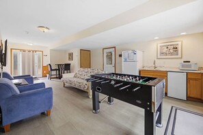 Een woonkamer met een tafelvoetbalspel, een bank, een salontafel, en een keuken met een koelkast en magnetron.