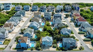 Vue aérienne d’un quartier résidentiel situé sur la côte, avec des maisons, une plage et une piscine.
