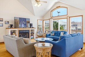 Un salon spacieux avec une cheminée, un canapé bleu, un canapé gris, une table basse ronde et un ventilateur de plafond.
