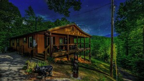 A wooden cabin with a porch, surrounded by trees and a clear night sky. - Cozy Bear Camp - Beautiful Views, Outdoor Hot tub, Firepit + More! (Sevierville)
