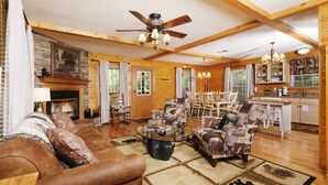 A spacious living room with a fireplace, wooden furniture, and a dining area with a chandelier. - Cozy Bear Camp - Beautiful Views, Outdoor Hot tub, Firepit + More! (Sevierville)