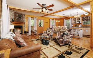 A spacious living room with a fireplace, wooden furniture, and a dining area with a chandelier. - Cozy Bear Camp - Beautiful Views, Outdoor Hot tub, Firepit + More! (Sevierville)