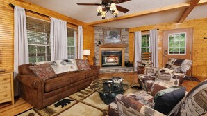 A cozy cabin interior with a fireplace, wooden walls, a sofa, armchairs, and a coffee table. - Cozy Bear Camp - Beautiful Views, Outdoor Hot tub, Firepit + More! (Sevierville)