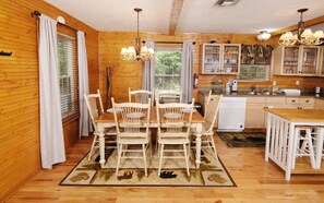 Een houten interieur met een eettafel, stoelen en een keukenhoek met kastjes en een koelkast.