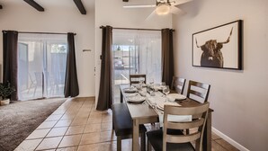 Un coin repas avec une table dressée pour quatre personnes, un ventilateur de plafond et un tableau encadré au mur.