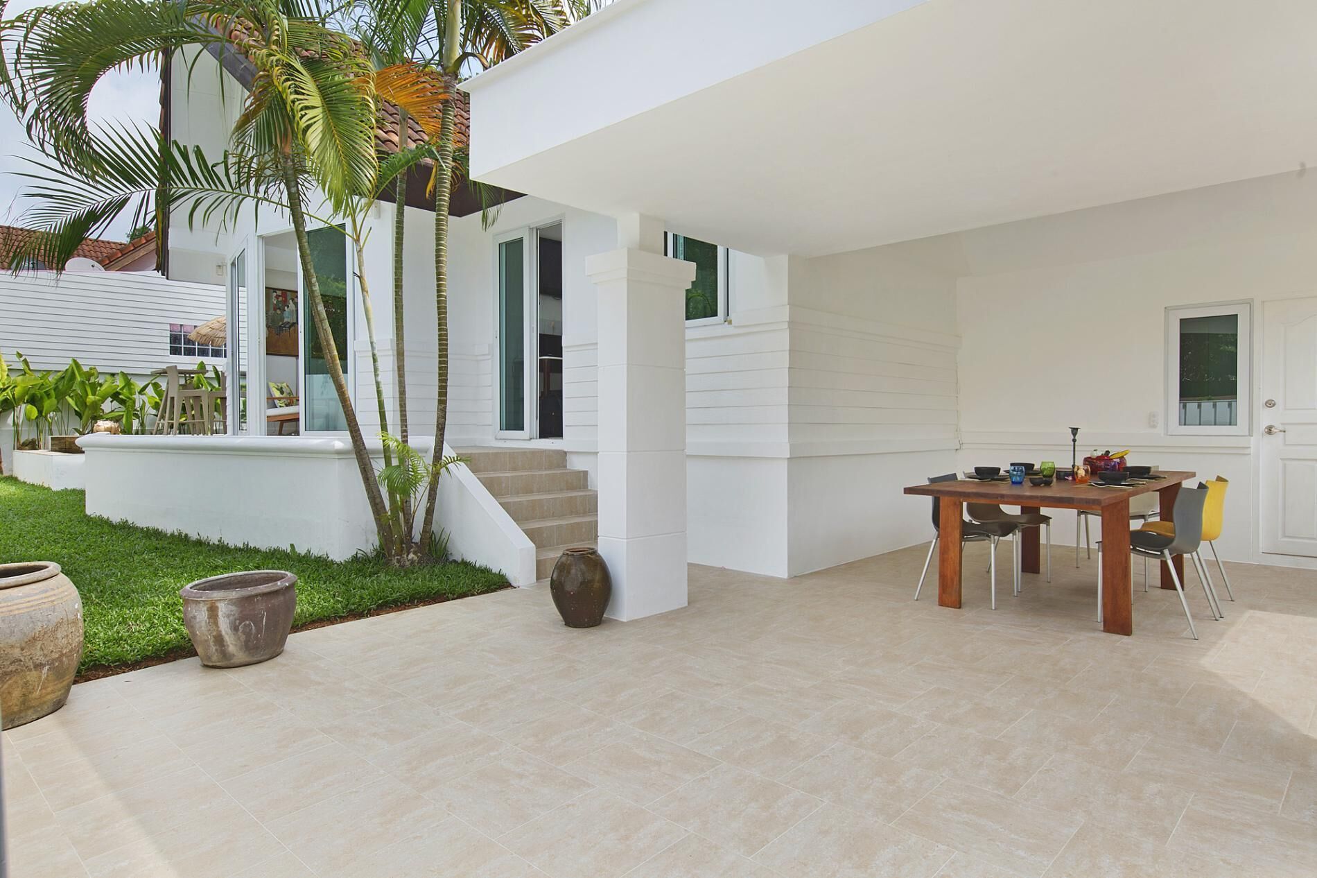 A modern house with a patio, a dining area with a table and chairs, and a staircase leading to the upper floor.