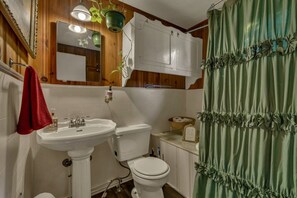 Un baño con lavamanos pedestal, inodoro y cortina de ducha verde.