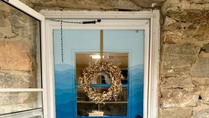 Eine blaue Tür mit Glasfenster und einem Kranz, in eine Steinmauer eingelassen.