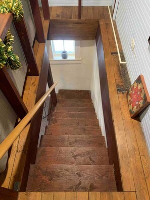 A wooden staircase with a handrail, a small window at the top, and a decorative cushion at the bottom.