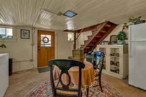 Un comedor con una mesa y sillas de madera, una cocina con refrigerador, y una escalera que lleva a un nivel superior.