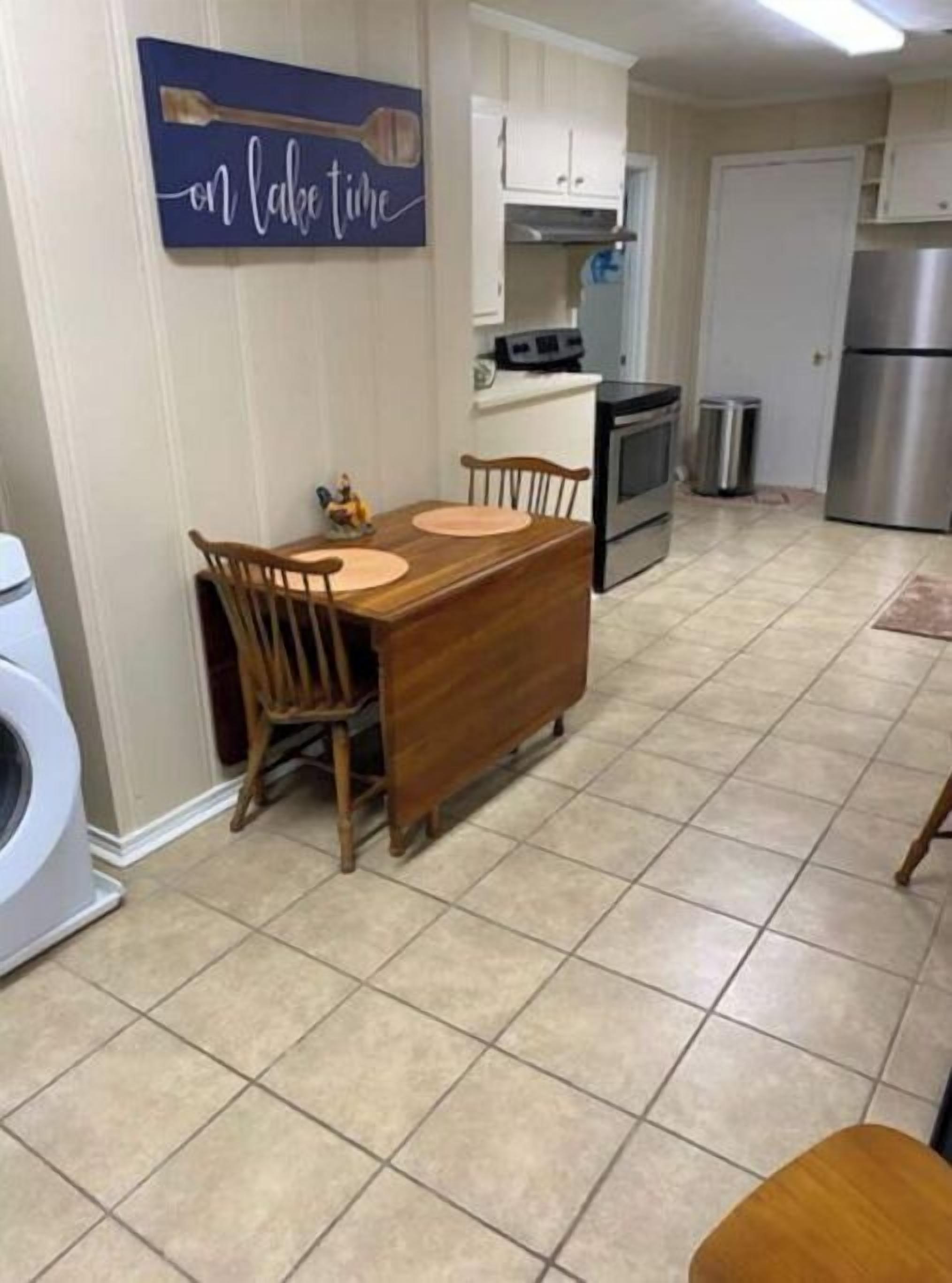 Uma cozinha com mesa de jantar, cadeiras, máquina de lavar, armários e uma geladeira de aço inoxidável.