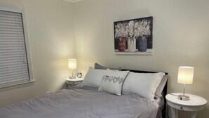 A bedroom with a bed, two bedside tables with lamps, a nightstand, and a painting on the wall. - Lida's Place - 3 BR 2 BA Ranch House - 7.6 miles to Grenada Lake (Grenada)
