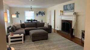 A living room with a sectional sofa, ottoman, fireplace, and a dining area with a table and chairs. - Lida's Place - 3 BR 2 BA Ranch House - 7.6 miles to Grenada Lake (Grenada)