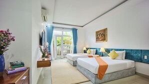 A hotel room with two beds, a desk, a chair, a TV, a window with curtains, and a painting on the wall. - Nelly Villa  | Copia Villa Hoi An (Thành phố Hội An)