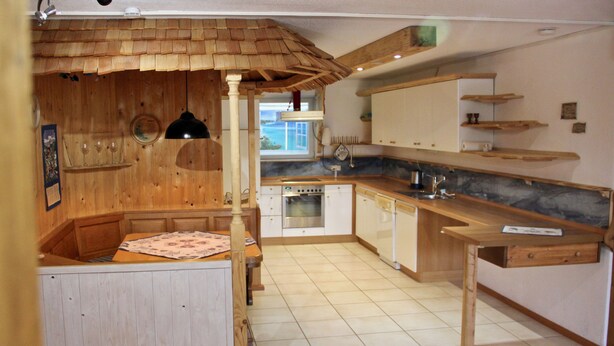 A kitchen with wooden cabinets, a built-in oven, and a dining area with a bench. - Charmante Ferienwohnung Handweberei mit Garten und Liegewiese, Wlan, 130 qm, Parkplatz (Saaldorf-Surheim)