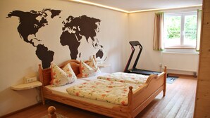 A bedroom with a wooden bed, a world map on the wall, a treadmill, and a window with curtains. - Charmante Ferienwohnung Handweberei mit Garten und Liegewiese, Wlan, 130 qm, Parkplatz (Saaldorf-Surheim)