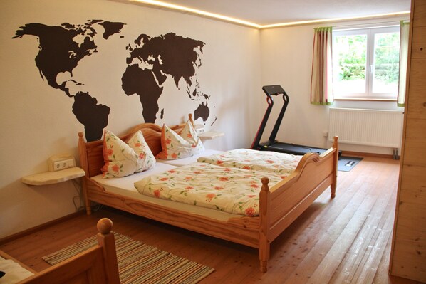 Un dormitorio con una cama de madera, un mapa mundial en la pared, una cinta de correr y una ventana con cortinas.