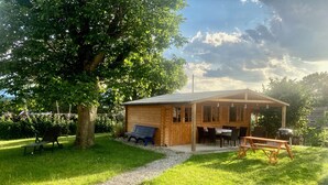 A wooden cabin with a gravel path leading to it, surrounded by lush greenery and a large tree. - Charmante Ferienwohnung Handweberei mit Garten und Liegewiese, Wlan, 130 qm, Parkplatz (Saaldorf-Surheim)